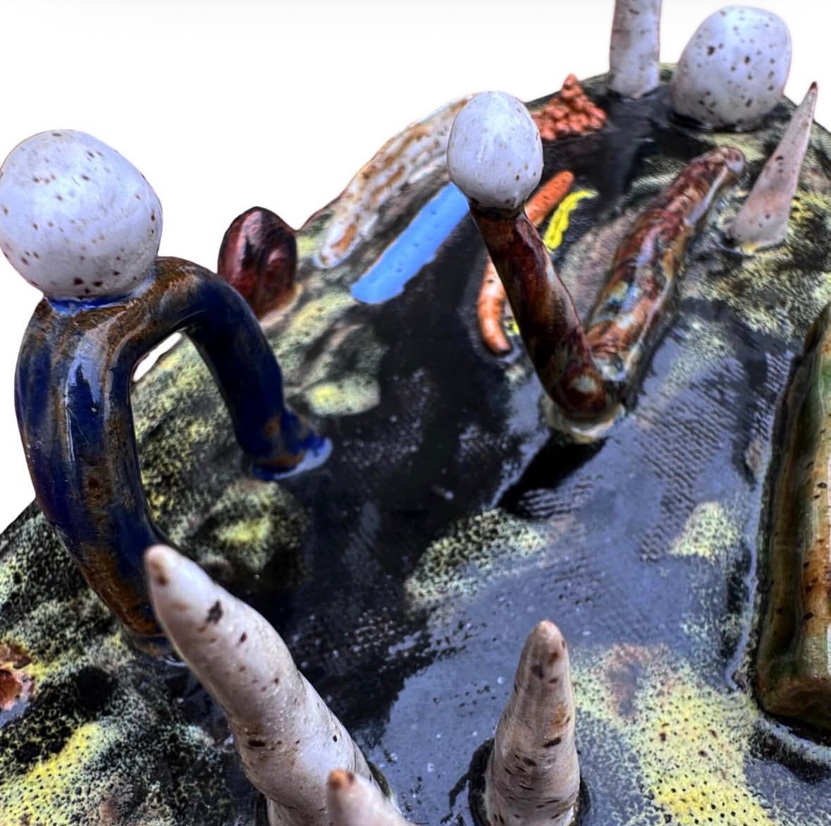 Close-up detail of ceramic landscape sculpture showing arched figures with white-sphere heads and spires